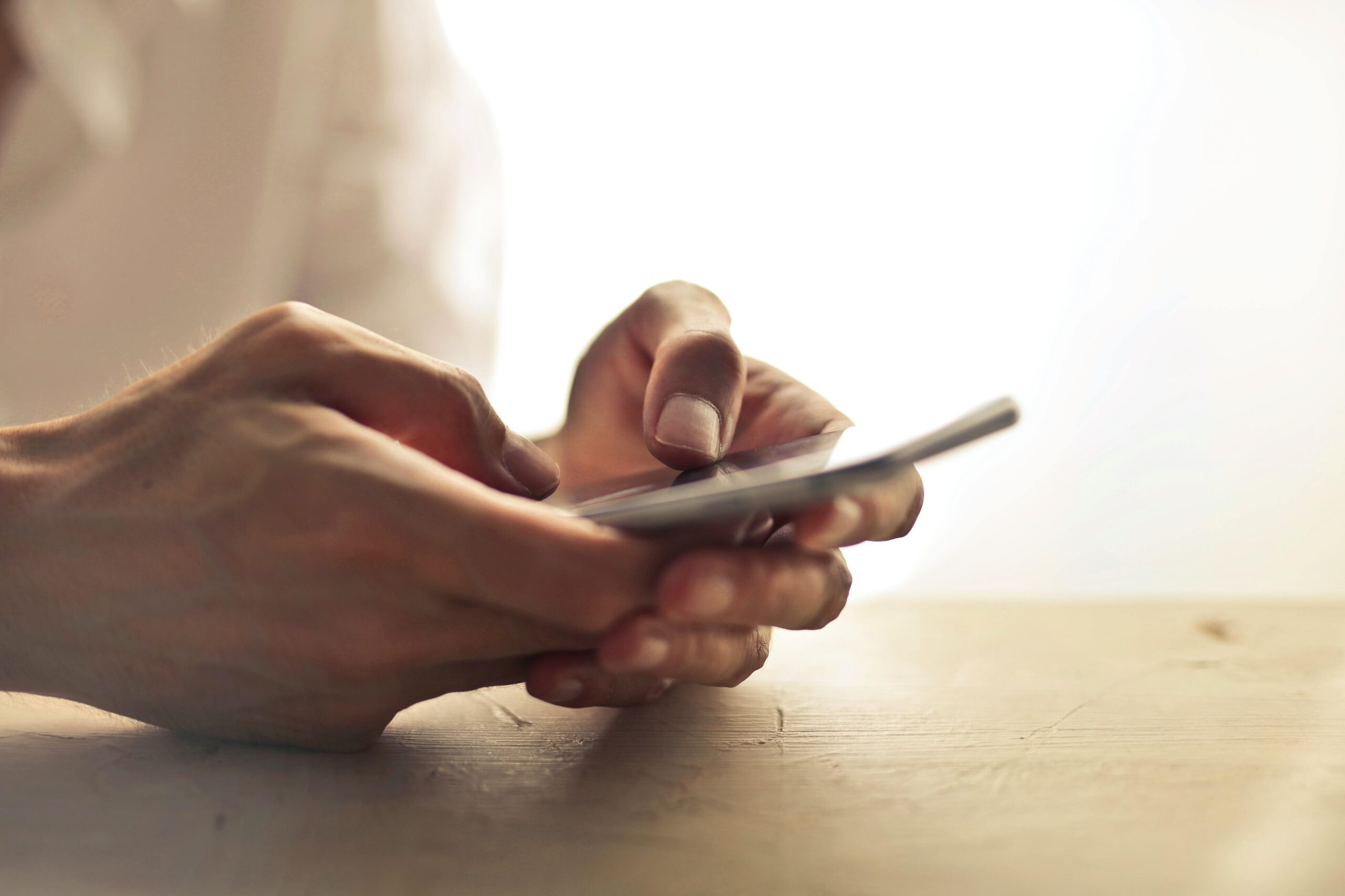 Close-up of an individual's hands holding a smartphone on a table indoors.