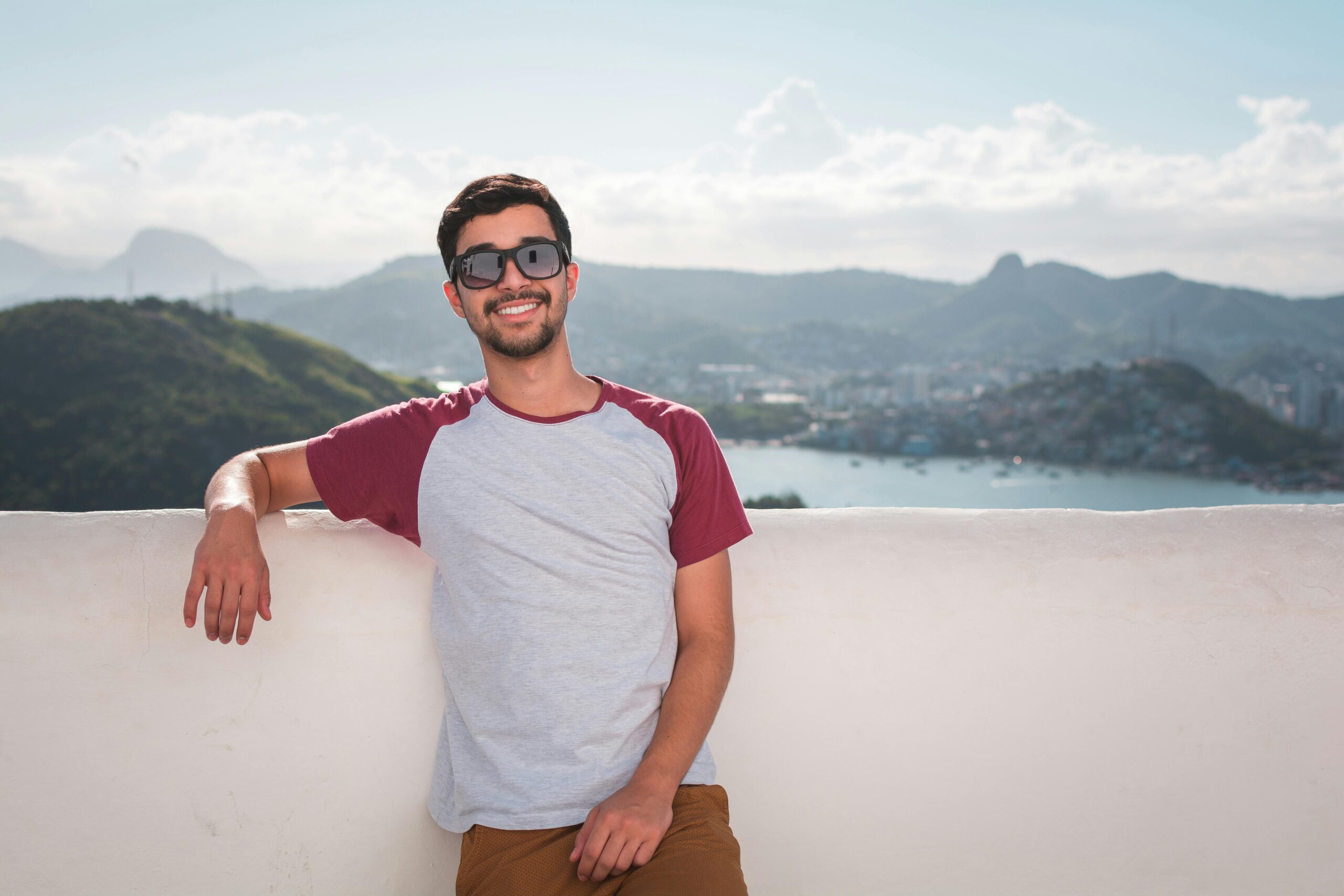 Digital Marketing Agency In Agra Young man in sunglasses leaning on a balcony with a scenic city view in the background.