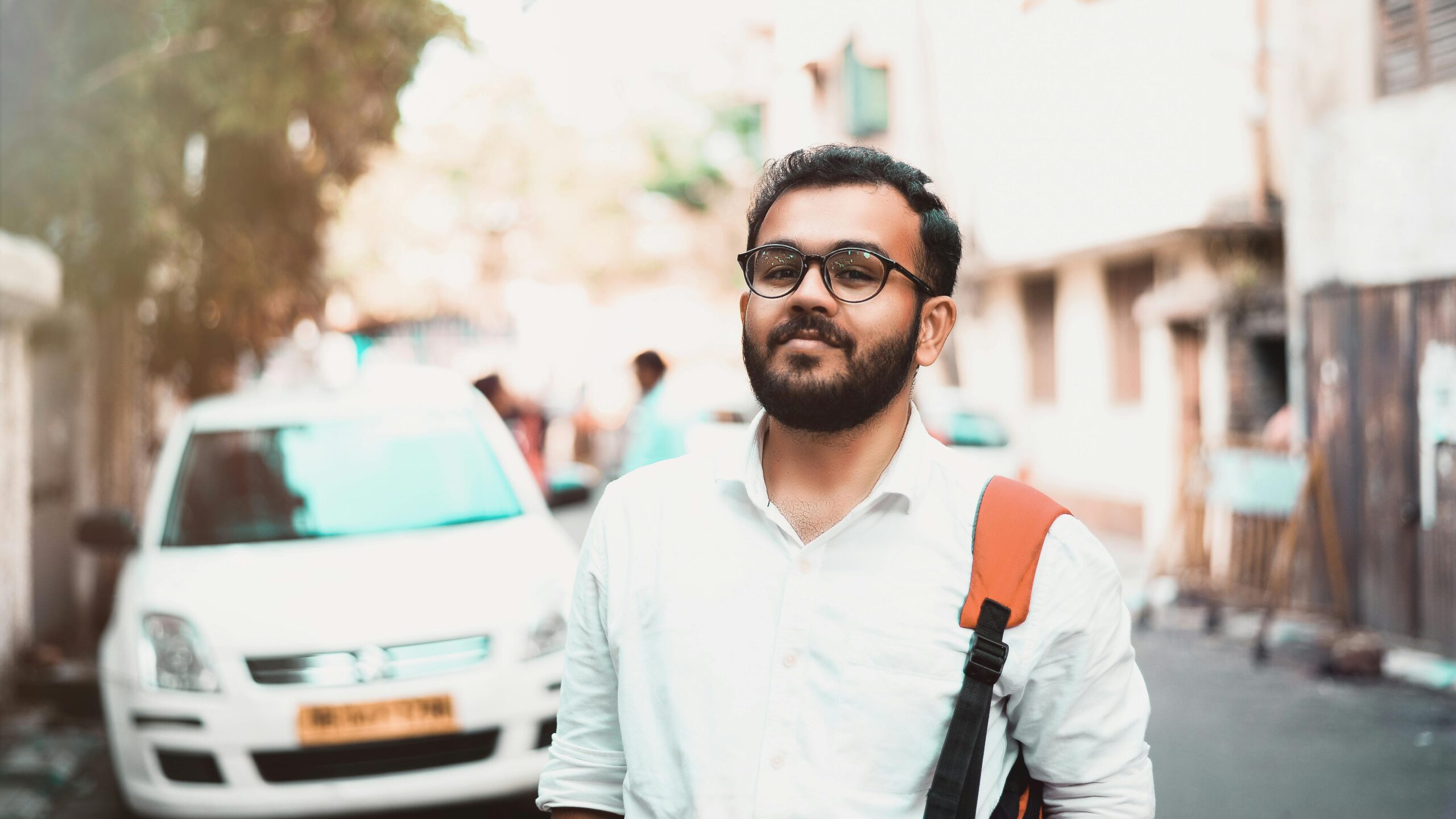 Digital Marketing Agency In Agra Confident man with glasses and backpack on a sunny urban street with cars in the background.